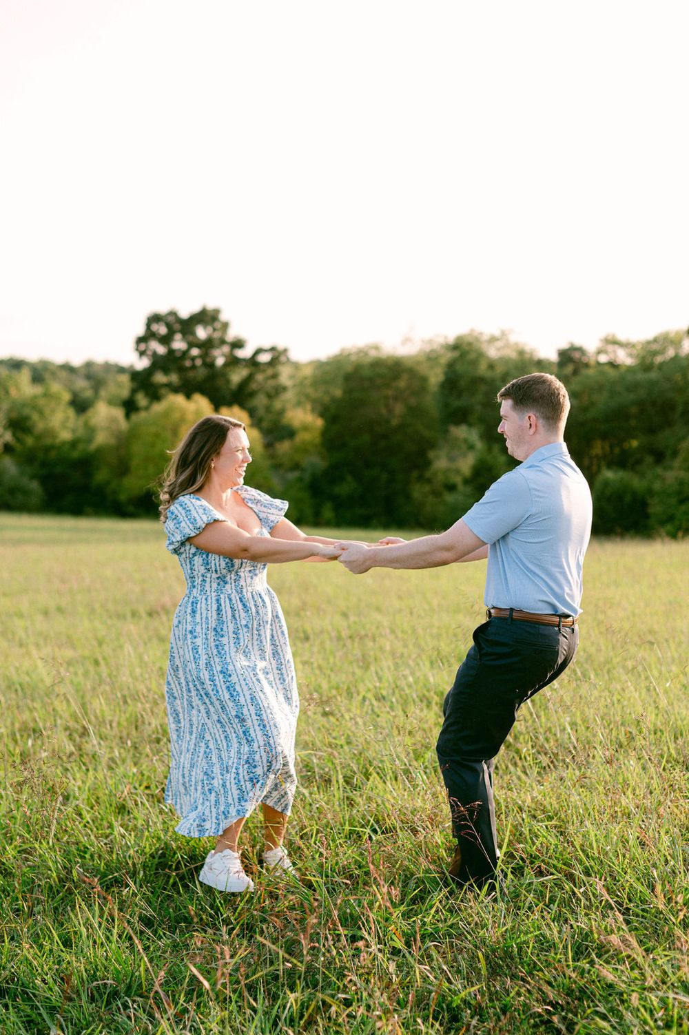 A couple dances playfully together in a sunlit grassy field during golden hour.