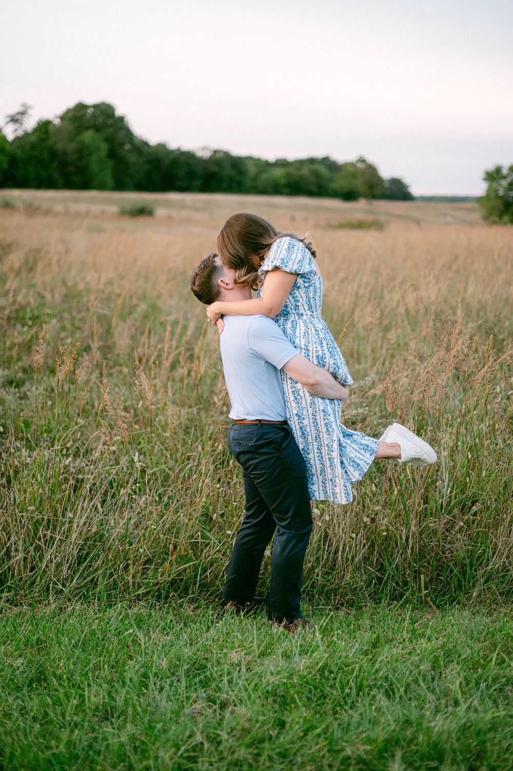 A playful couple embraces and dances together in a field of tall grass during a summer photo session.