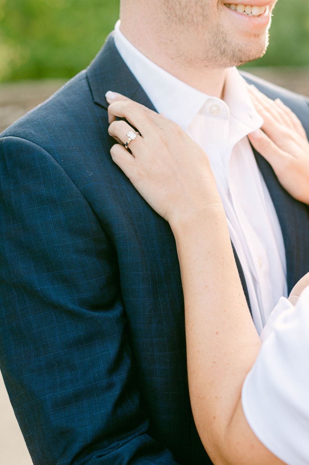 Close up of hands resting on a navy suit jacket showing a wedding ring detail.