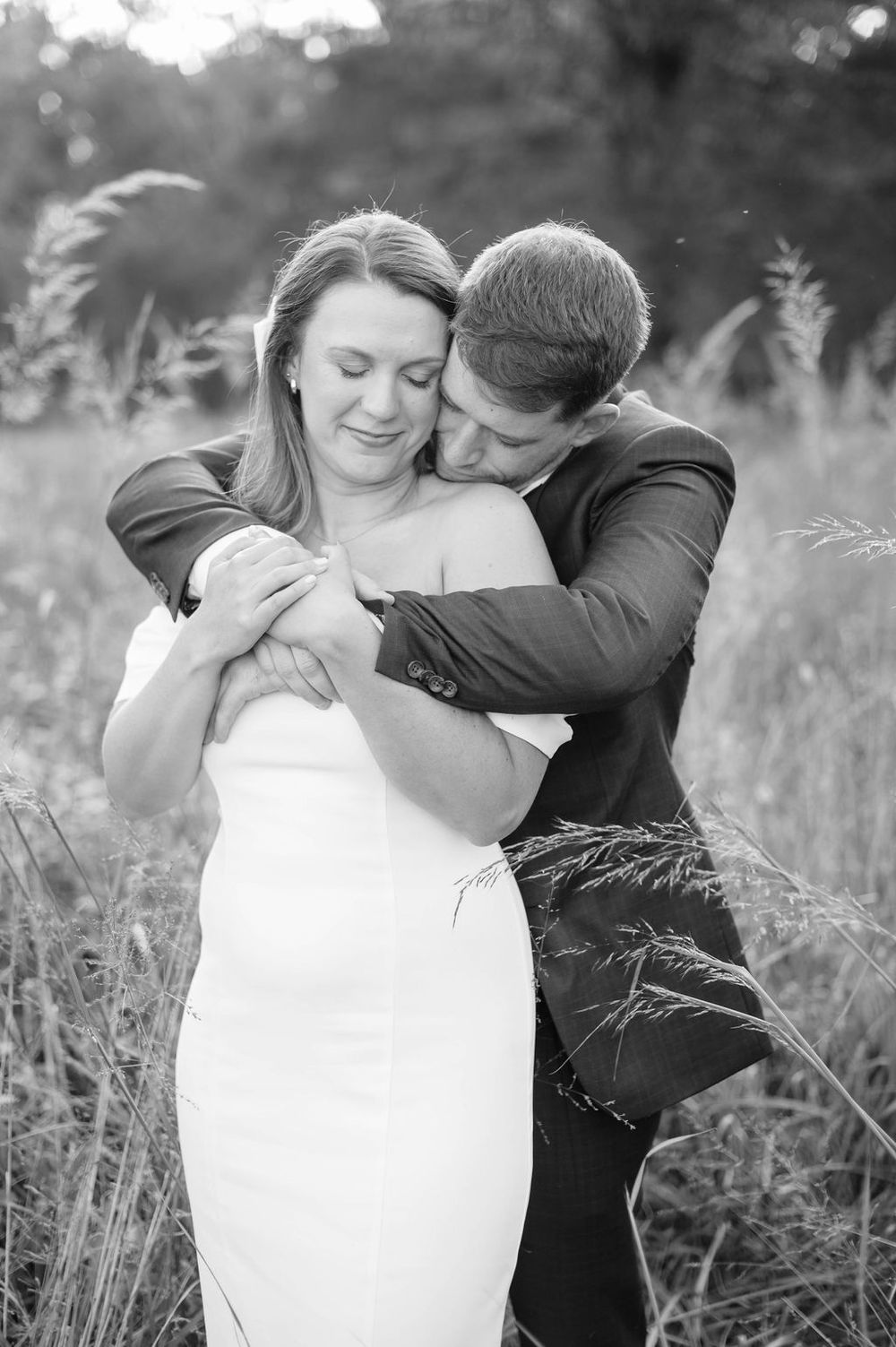 Romantic black and white photo series of a couple embracing in a field of tall grass.