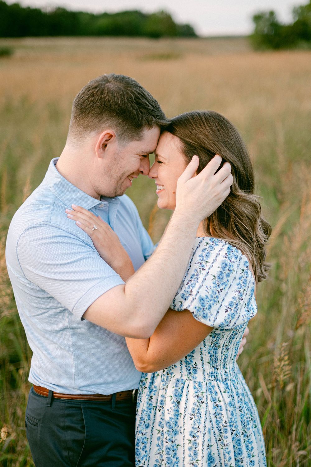 A couple embraces in a sun-lit field with tall grass, creating a romantic outdoor scene.