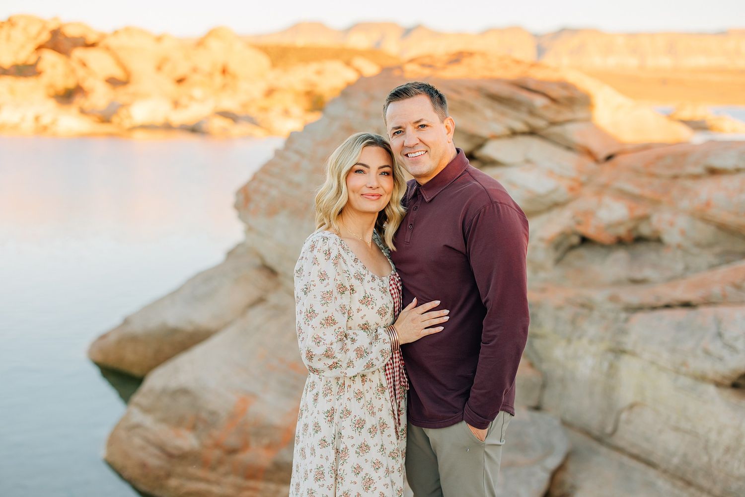 Couple embraces during sunset photoshoot among red rock formations in a desert landscape.