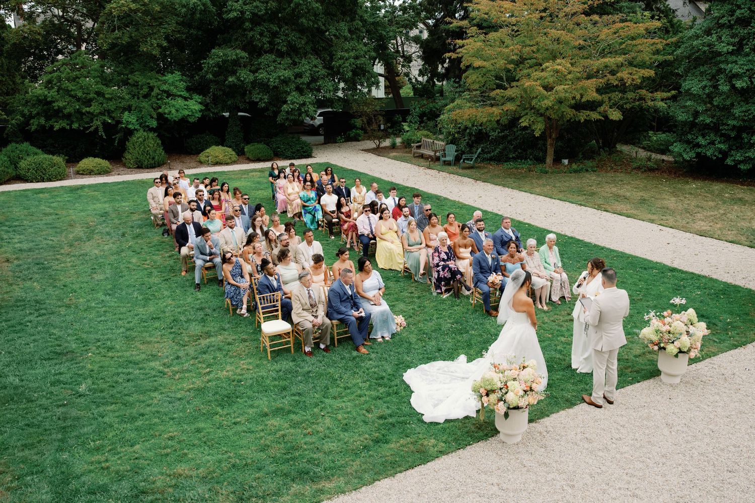 Wedding guests gather on a grassy lawn for an outdoor celebration at a garden venue.