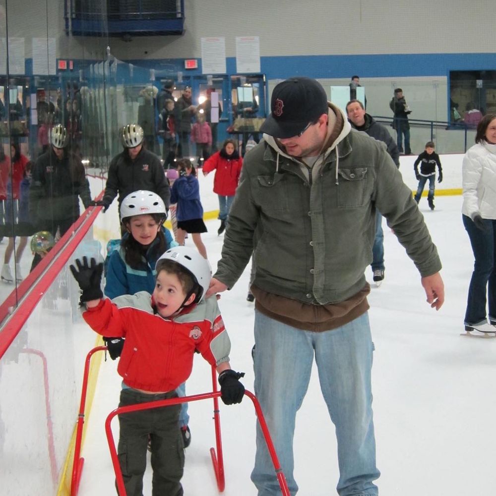 People learning to ice skate with assistance bars on indoor rink.