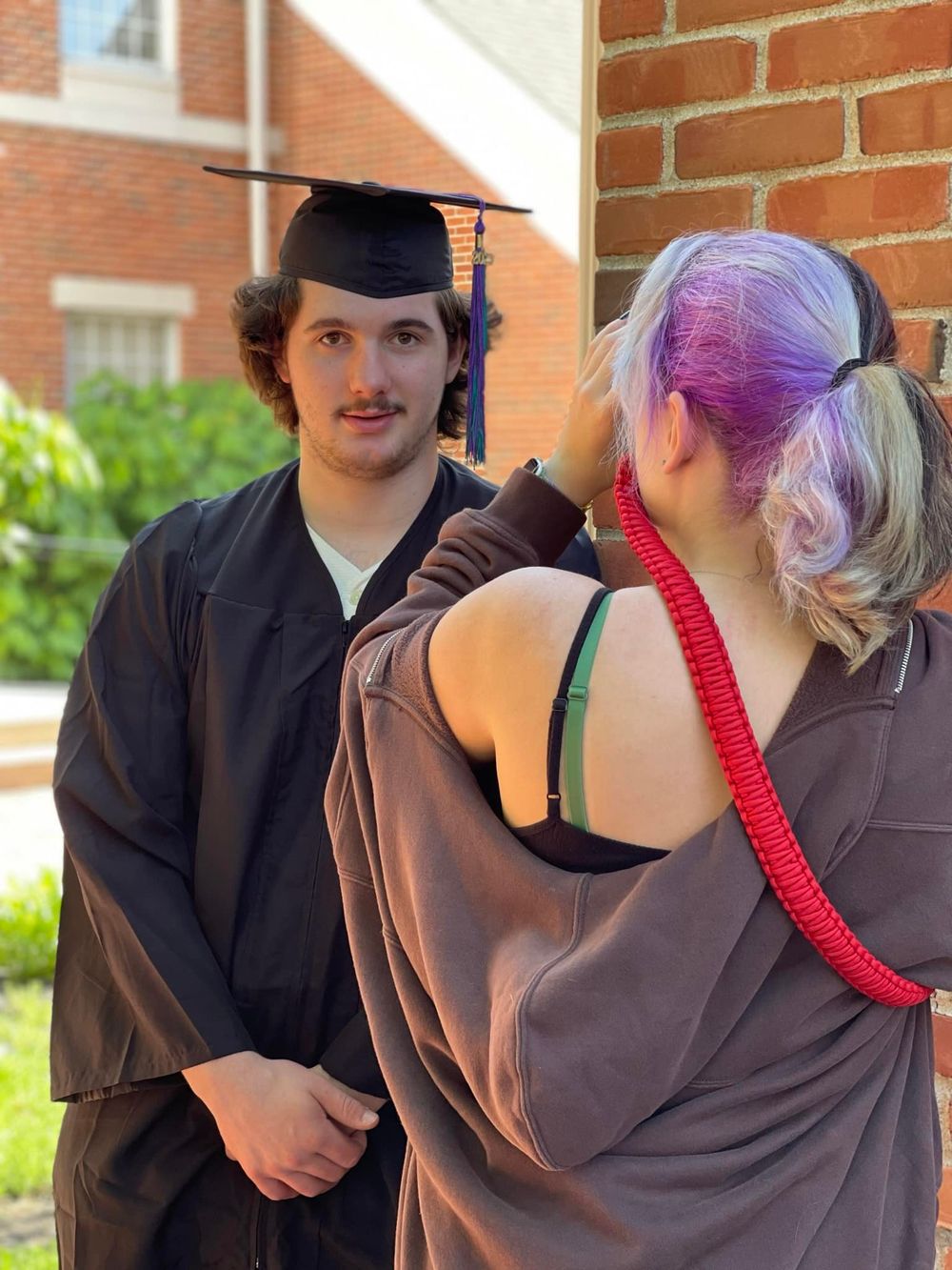 Group wearing graduation attire standing against brick wall outdoors.