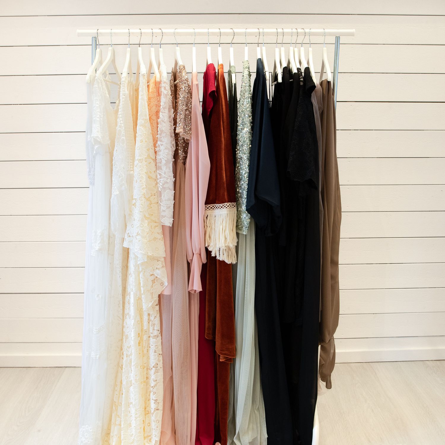 A clothing rack displaying a variety of maternity gowns in neutral, bold, and dark tones for photoshoots.