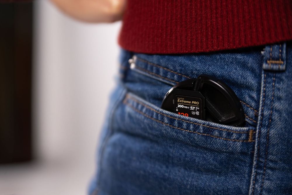 A black camera lens cap tucked into the front pocket of blue denim jeans.