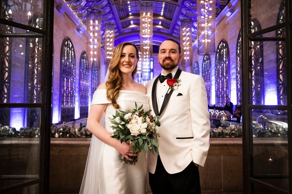 A couple poses at their wedding reception in Union Trust in an elegant venue with purple uplighting and ornate architectural details.