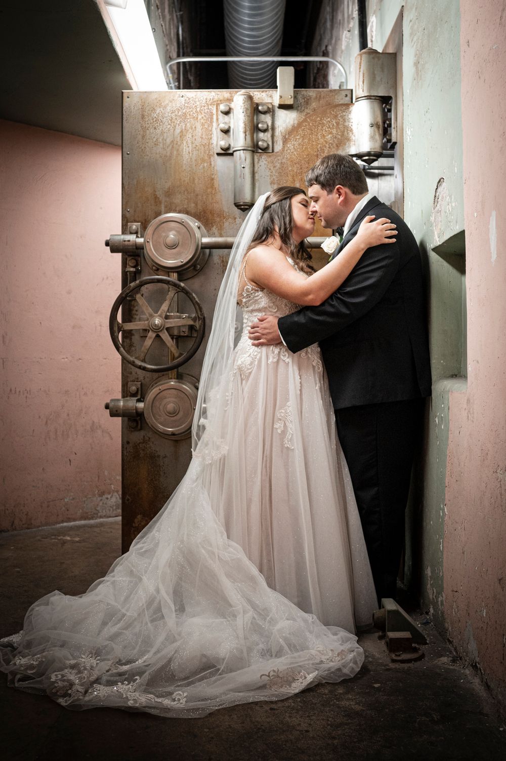 A romantic wedding couple shares intimate kisses in an industrial basement setting with vintage machinery in the background.
