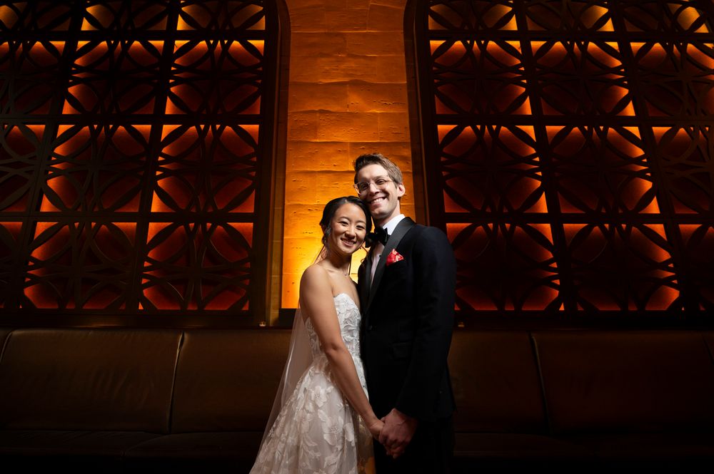 A couple shares a joyful moment in front of an ornate wooden wall panel with ambient lighting at Union Trust in Philadelphia