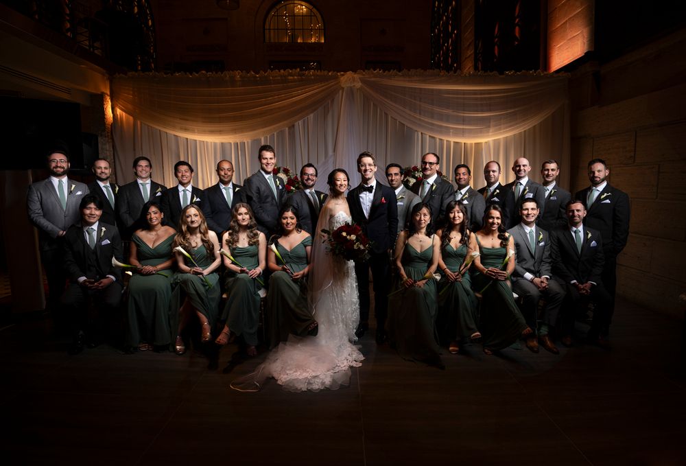 Elegant wedding party in formal attire poses for dramatic portrait in grand ballroom setting of Union Trust wedding in Philadelphia.