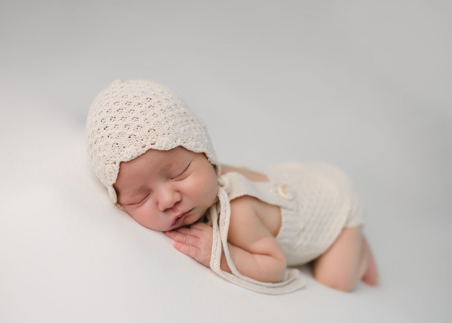 Blue-eyed baby boy sitting on a soft cream blanket during a light and airy studio photography session.