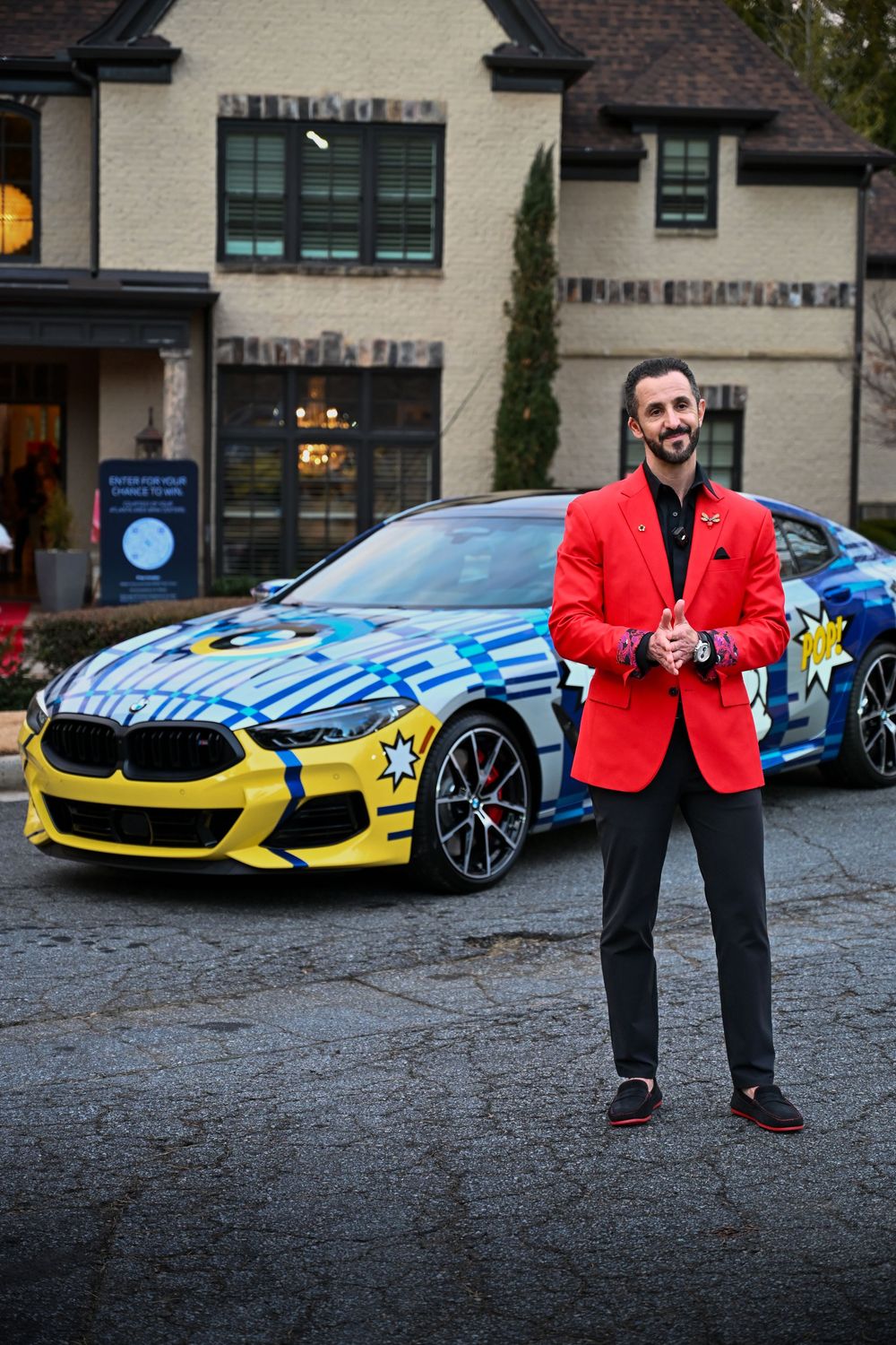 A bright red BMW M8 with custom blue and yellow paint sits outside a building.