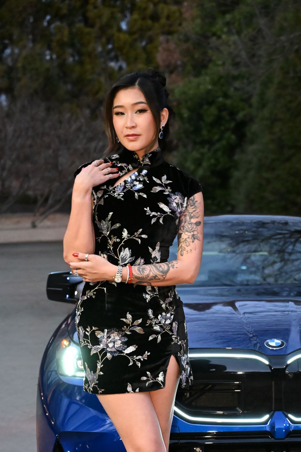 Elegant black velvet dress with floral embroidery photographed near a blue luxury car.