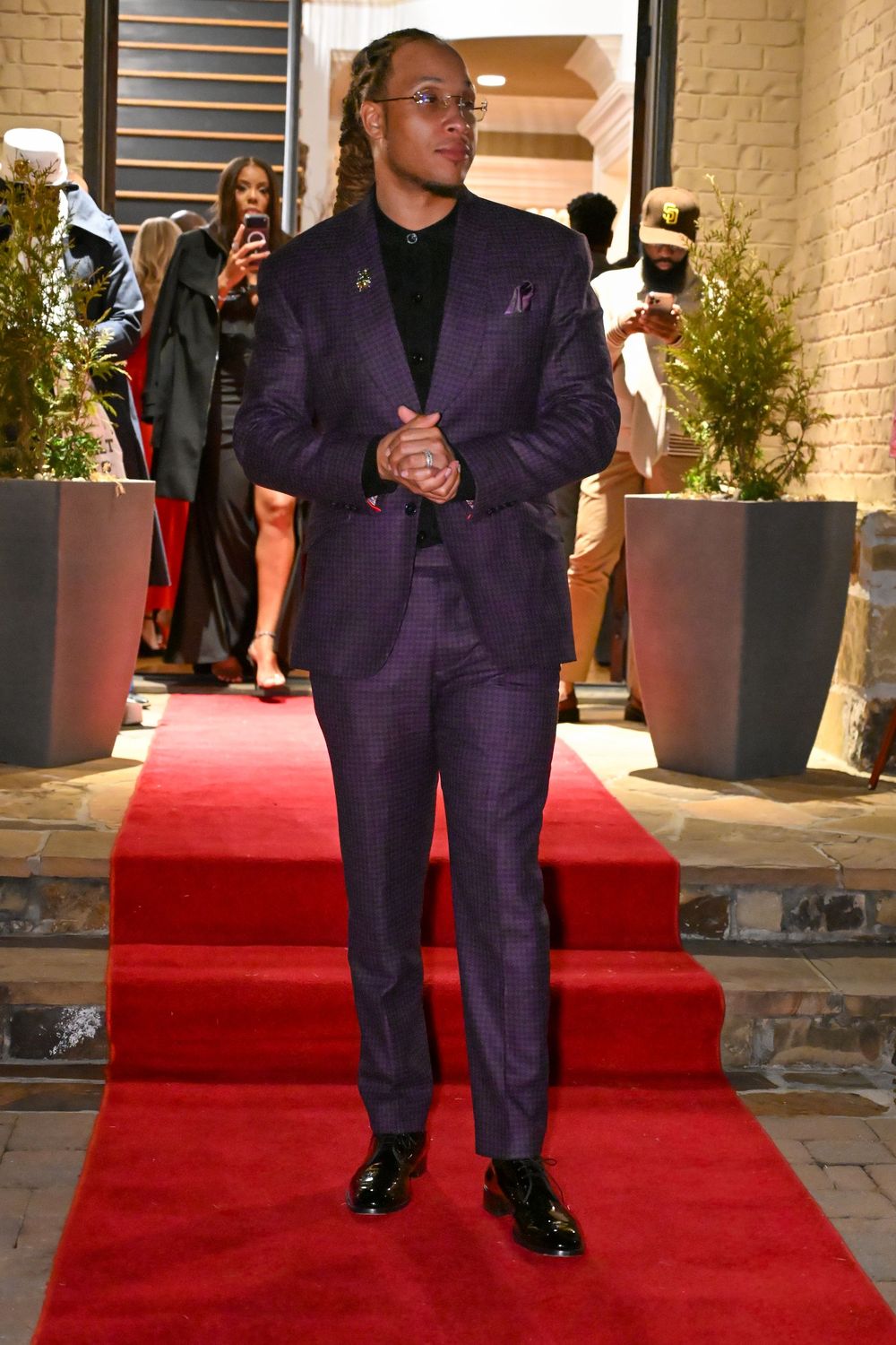 People in matching purple suits walk together on a red carpet at an elegant event entrance.
