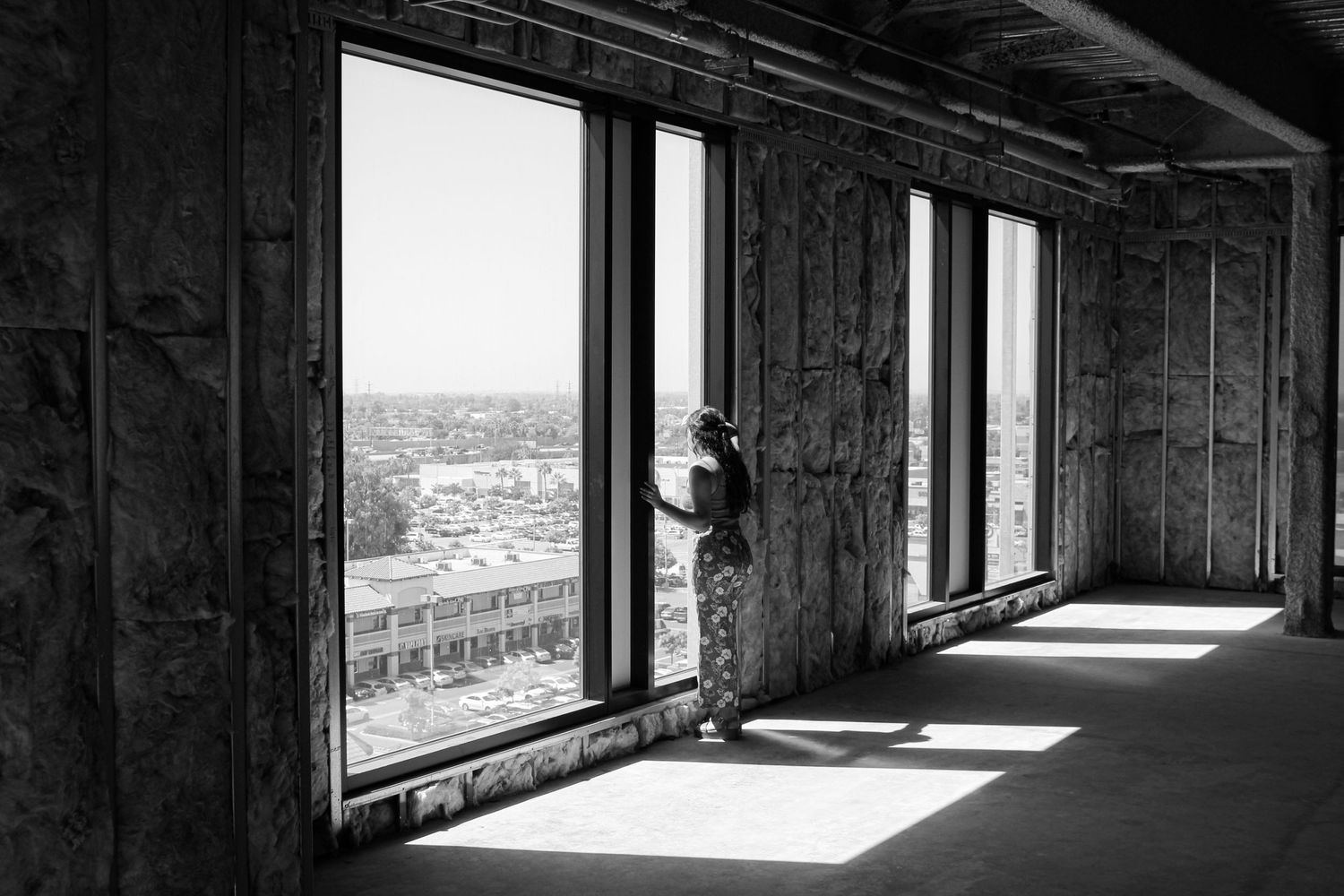 A woman looking out of a window from a building that is being constructed. The model for the photo shoot stands looking out over a city.