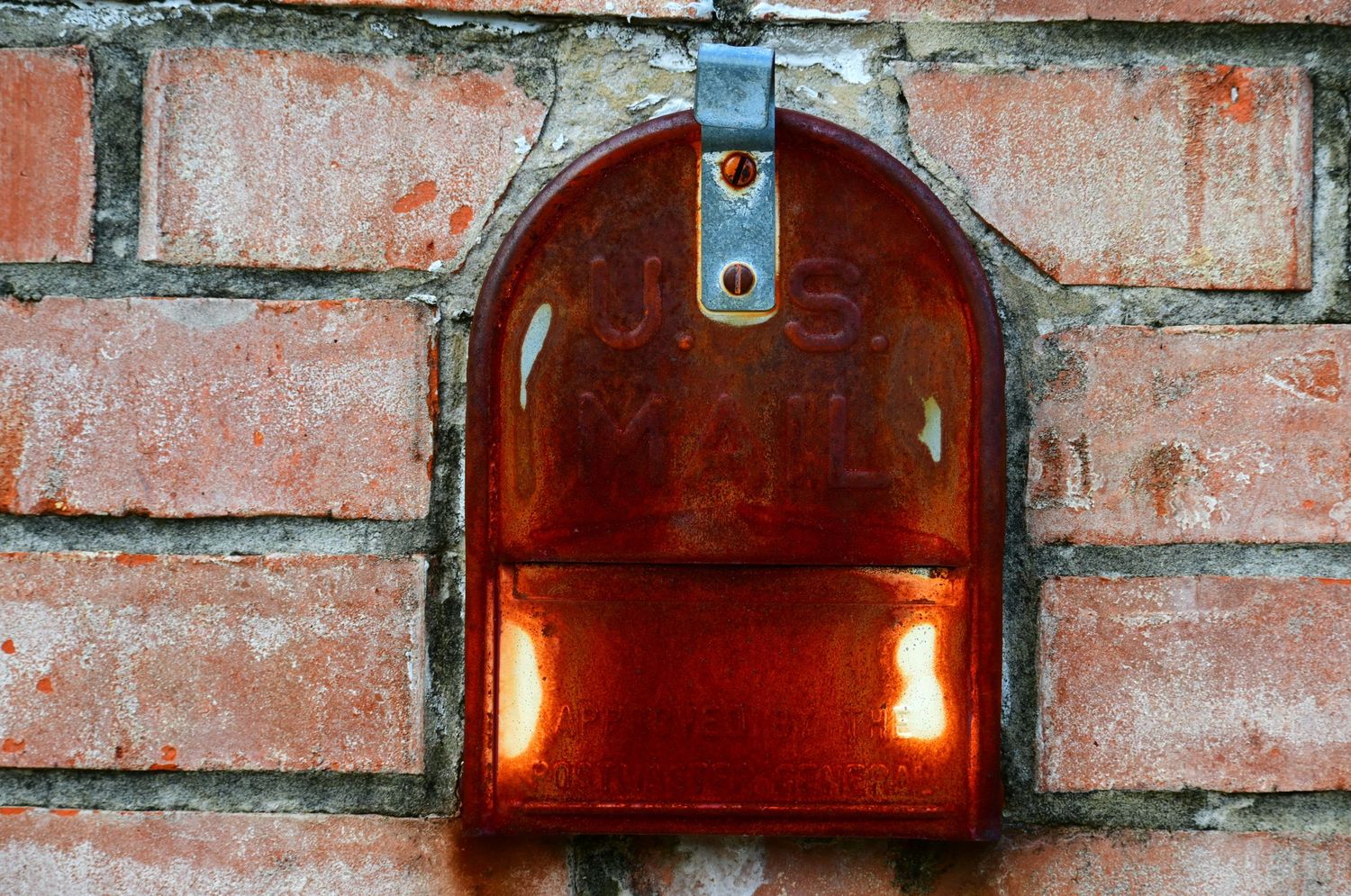 Rustic mailbox door in a brick frame.