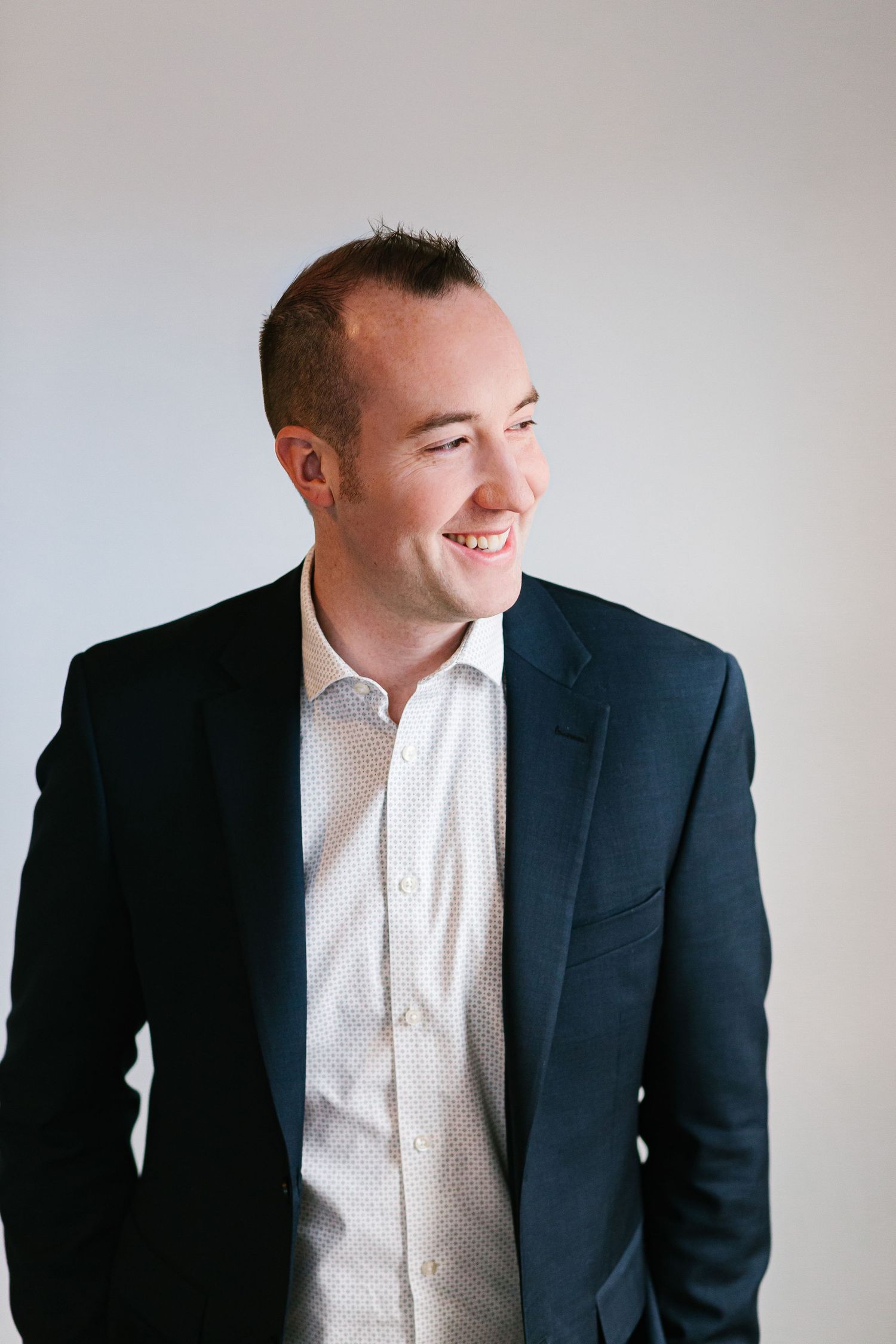 Professional smiling portrait of someone wearing a navy blazer and white polka dot dress shirt against light background.