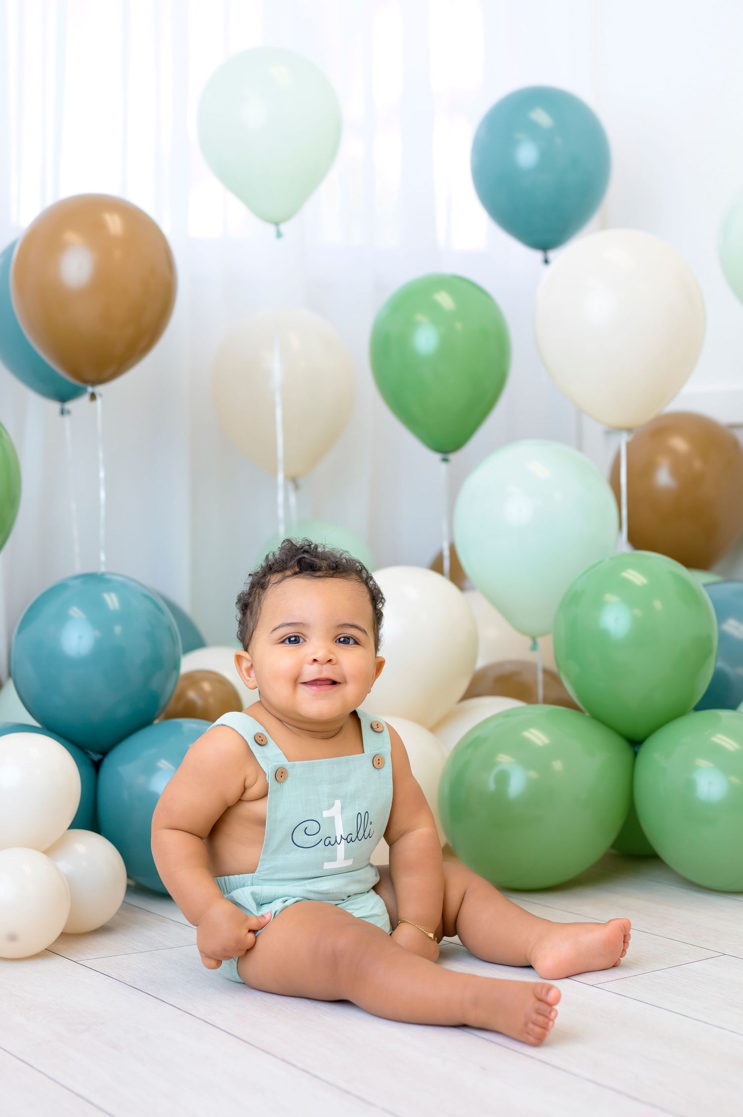 Colorful balloon arrangement featuring mint, teal, brown and white balloons creates festive backdrop for baby photo session.