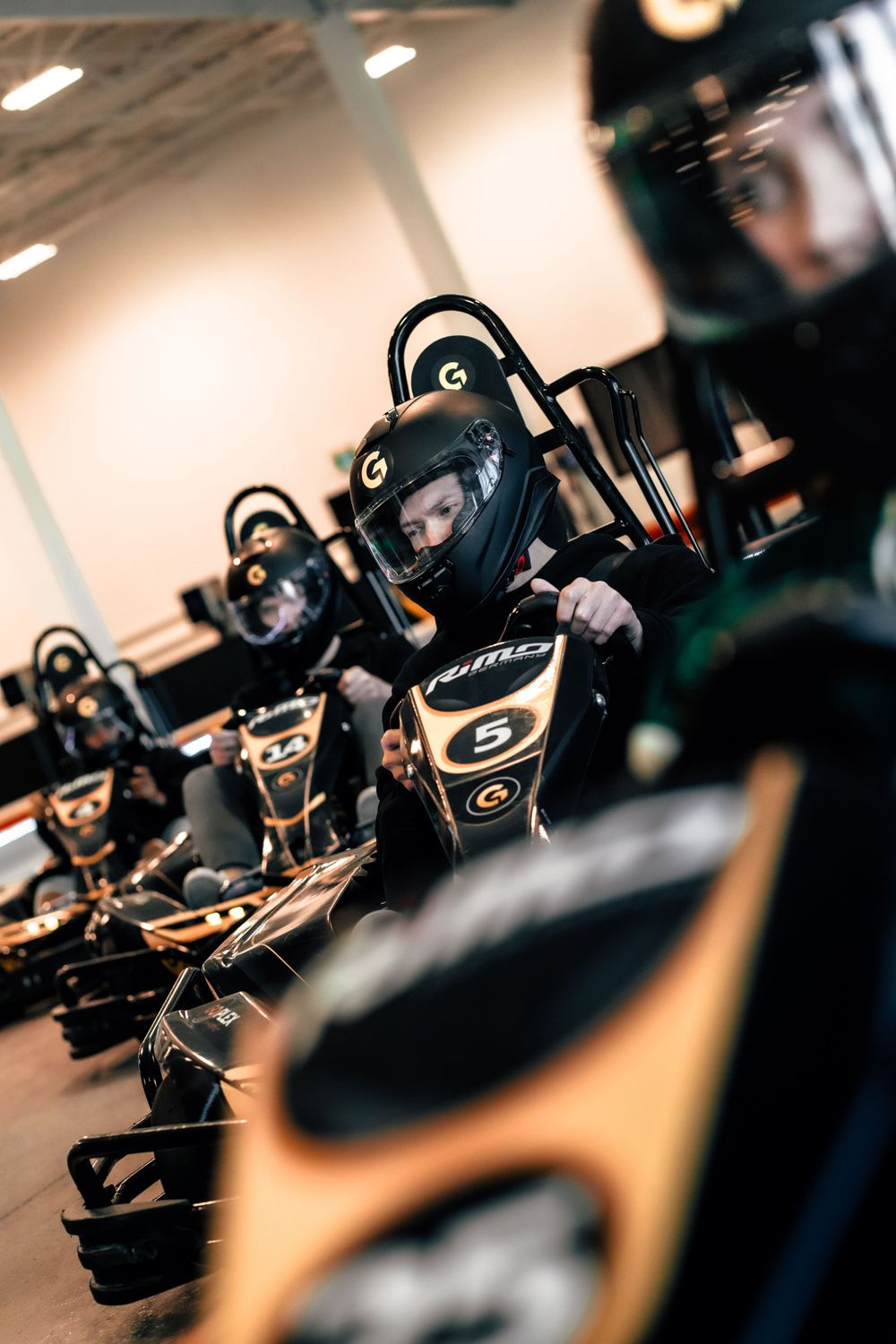 Row of go-karts with drivers in helmets lined up on an indoor track. Mtlshutter photography