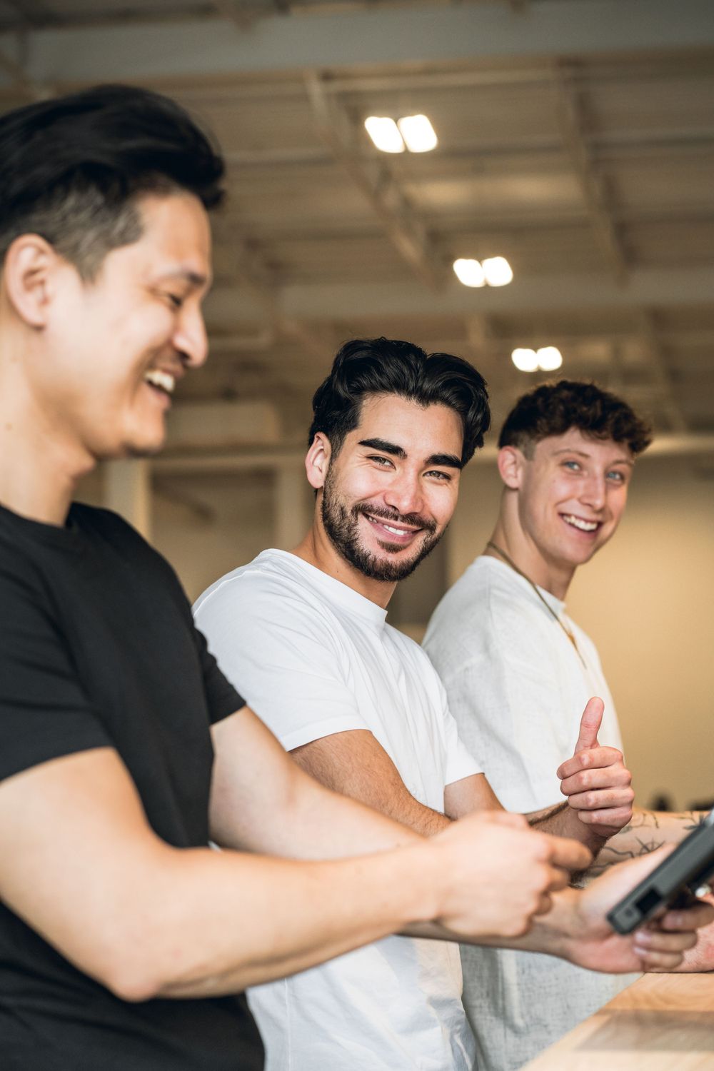 Three friends laughing together while looking at a mobile device in a bright indoor space. Mtlshutter photography