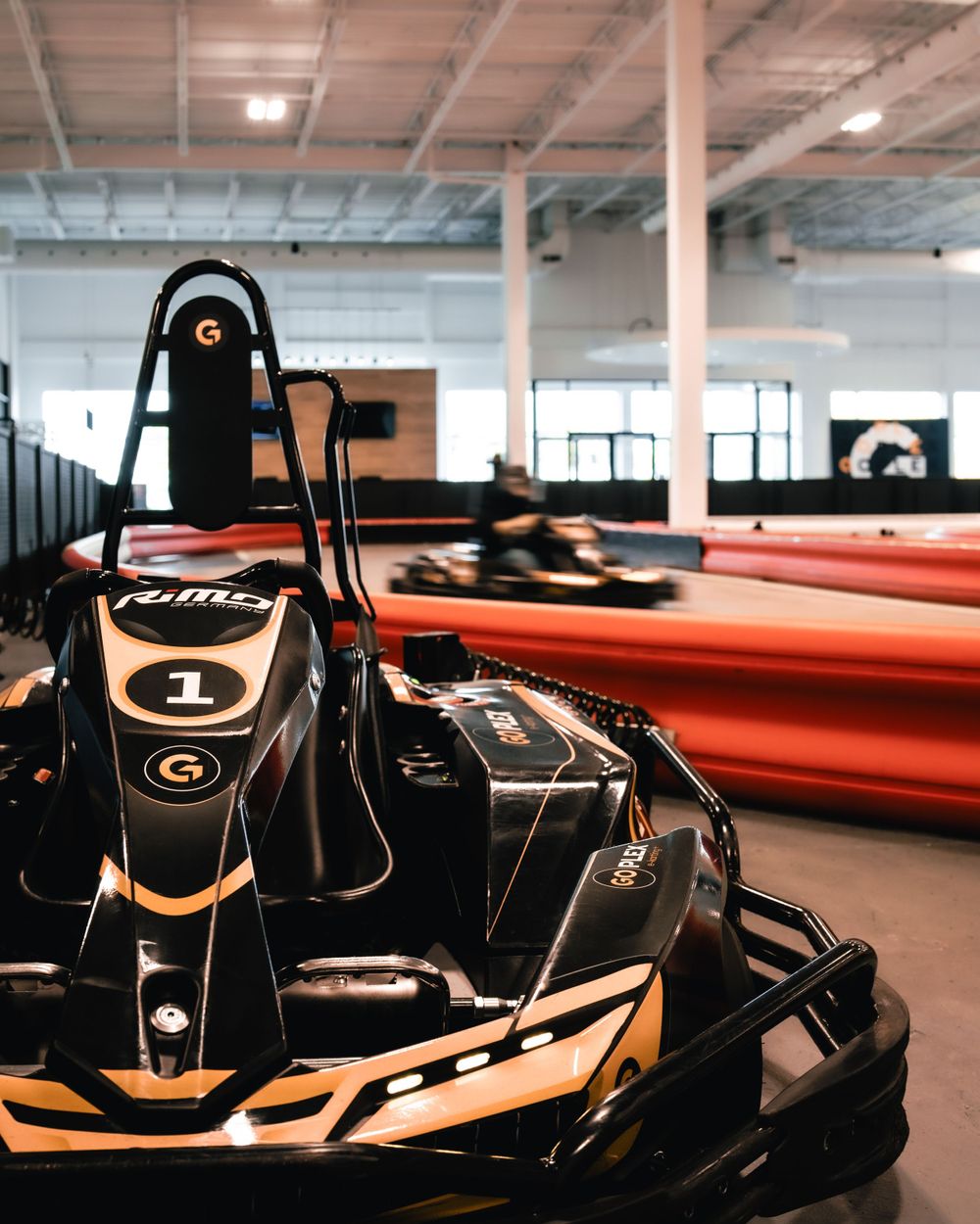 Close-up of a black and orange go-kart in an indoor racing facility with bright lighting. Mtlshutter photography