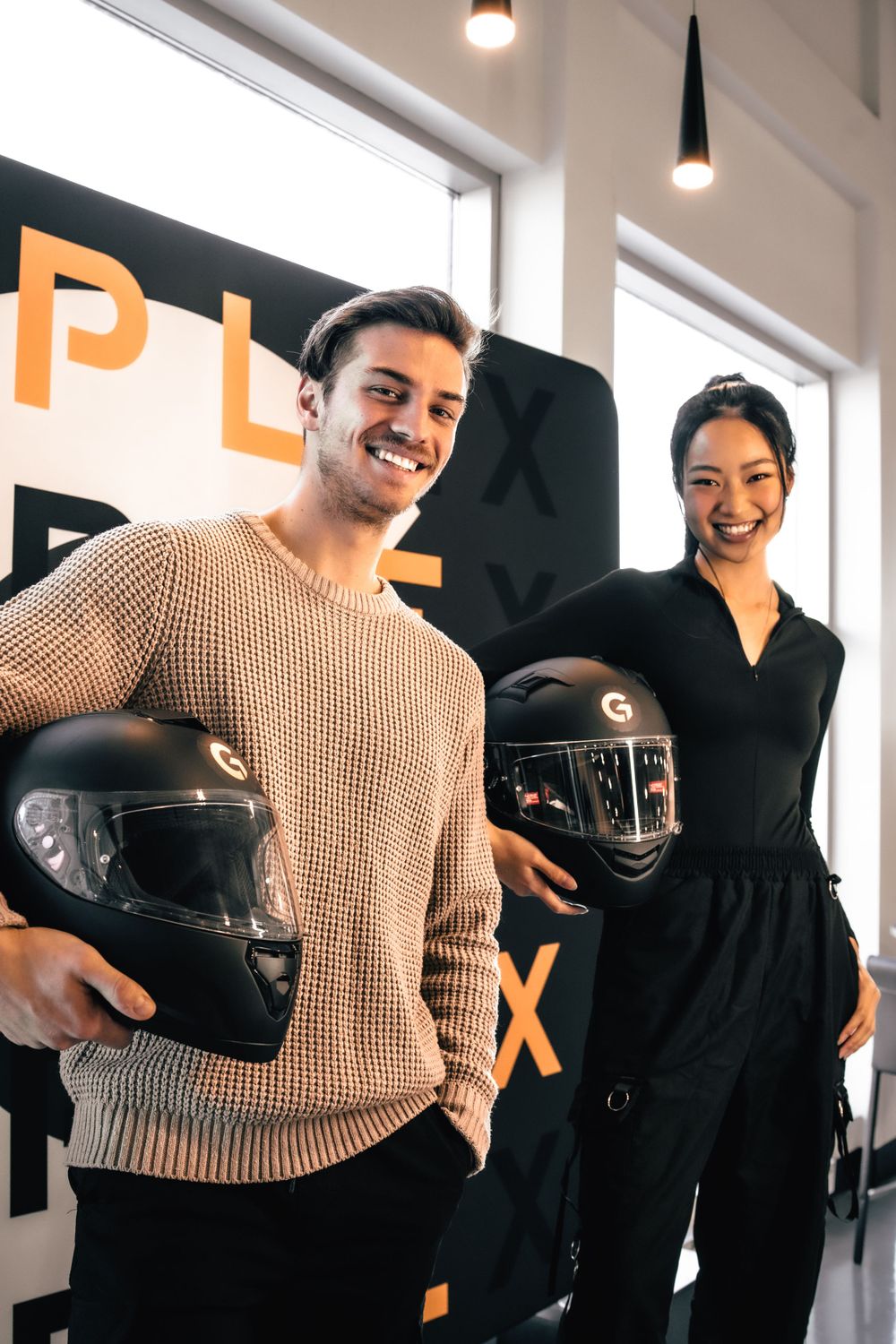 Two people posing with racing helmets in front of orange signage. Mtlshutter photography