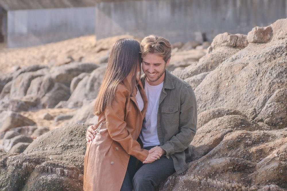 Couple shares intimate moment on rocky coastal outcrop during golden hour.