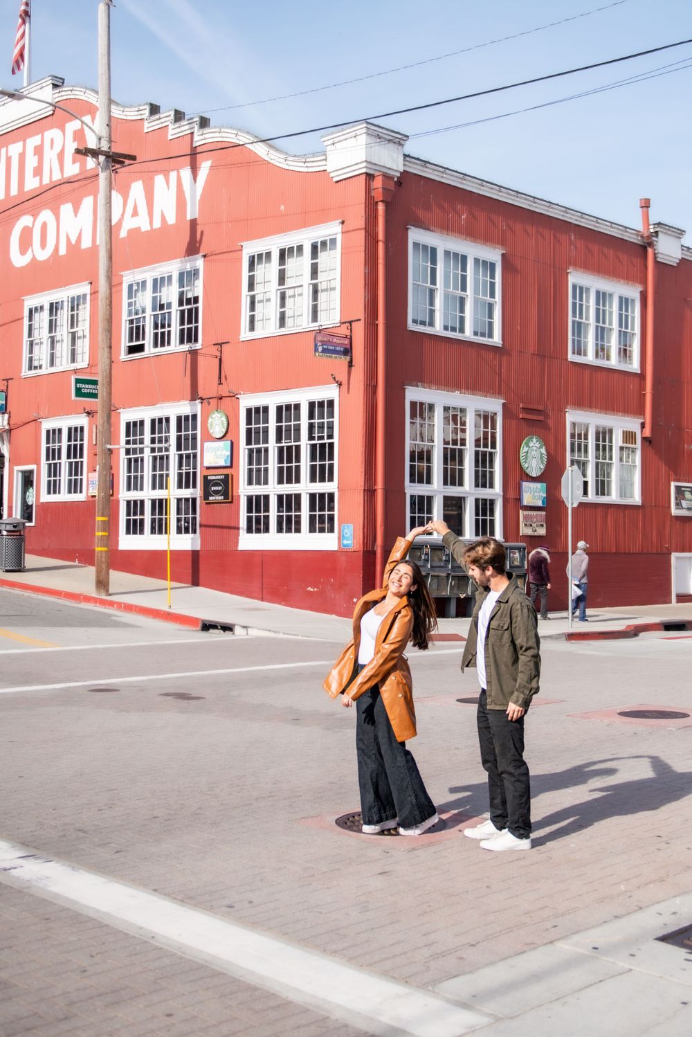Two people stand in front of a historic red brick building with large windows on a city street.