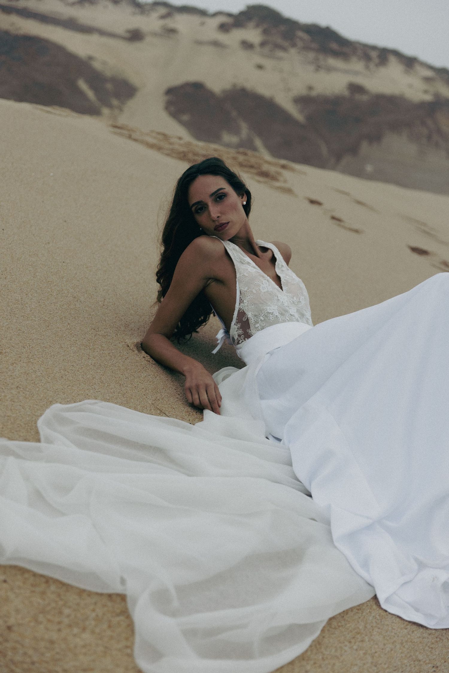 White wedding dress flowing across desert sand dunes in dramatic bridal portrait.