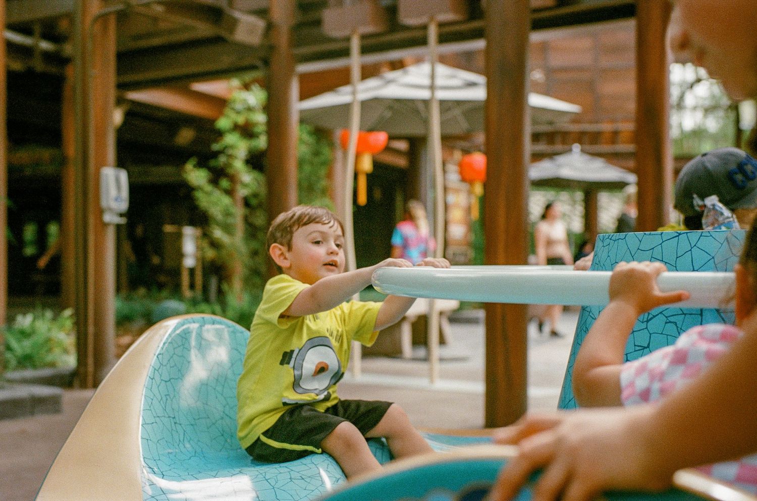 Young child enjoying a playground ride on a bright turquoise seat during a sunny day.