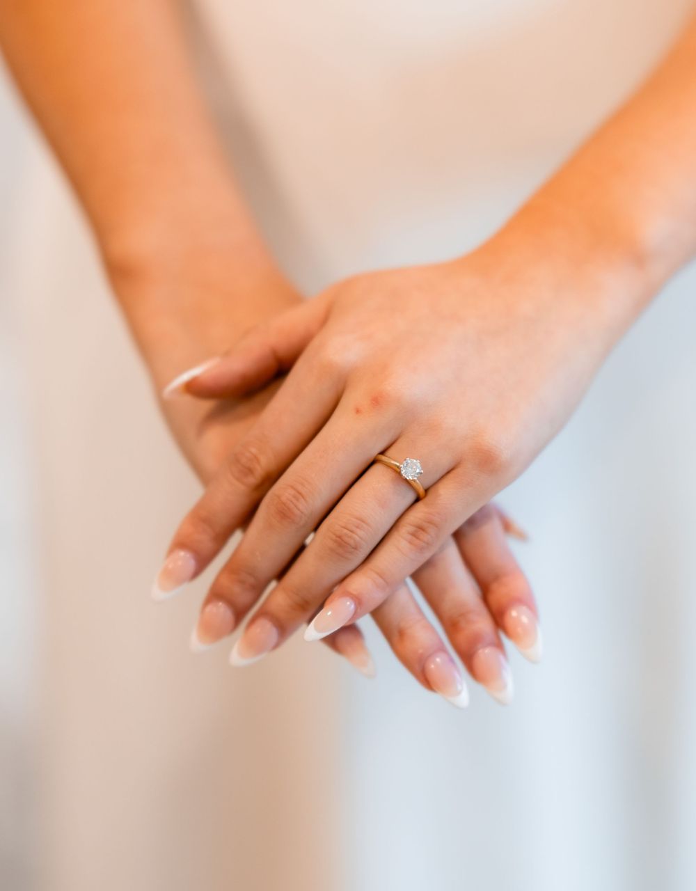 Close-up of hands displaying an elegant engagement ring with a sparkling diamond solitaire in natural light.