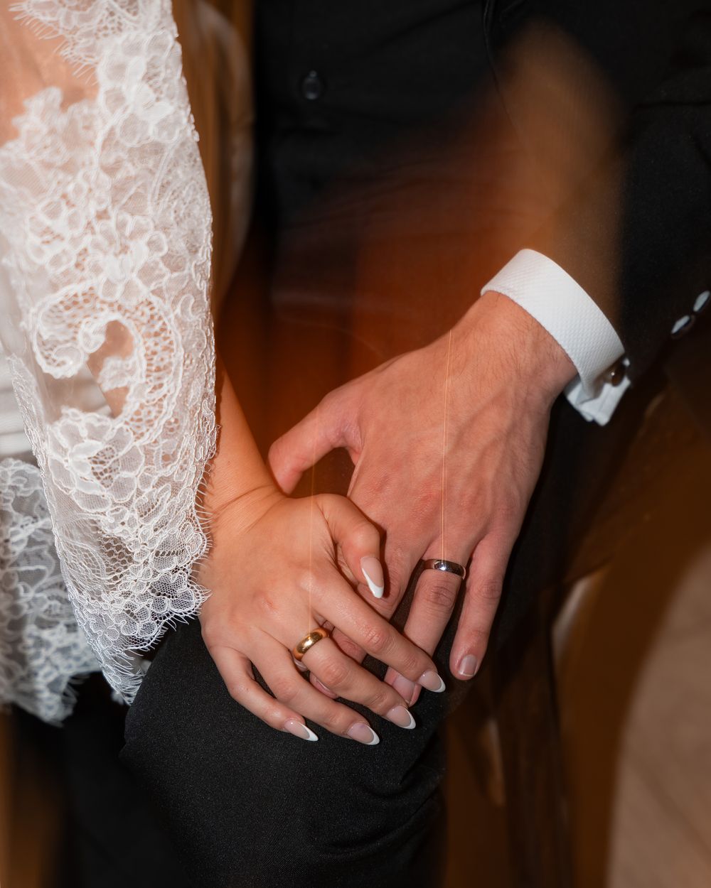 Close-up of newlywed couple's hands with wedding rings and delicate white lace dress detail.