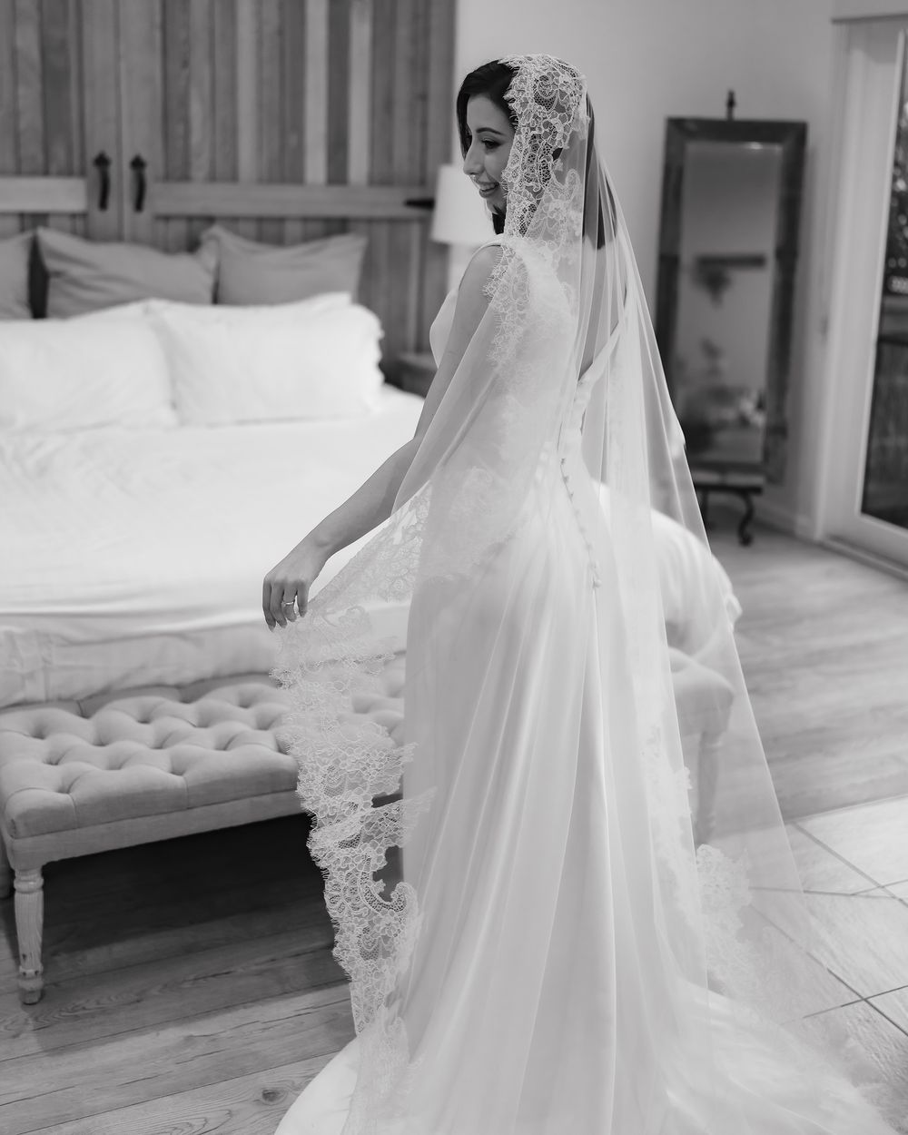 A bride in a flowing white wedding gown and veil stands gracefully in a bright indoor setting.