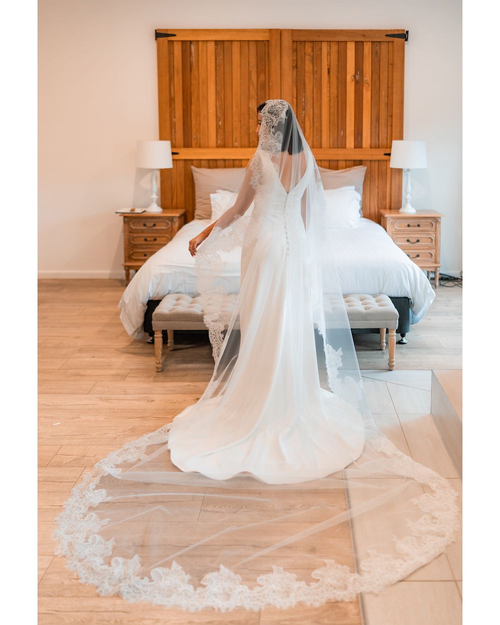 A flowing cathedral length veil with lace trim spreads across a wooden floor.