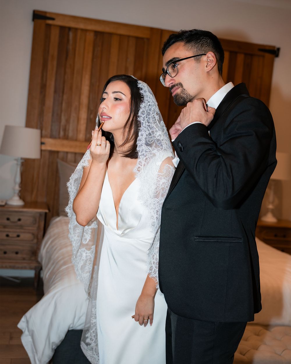 A couple in wedding attire share a lighthearted moment dancing and laughing together in a rustic indoor setting.