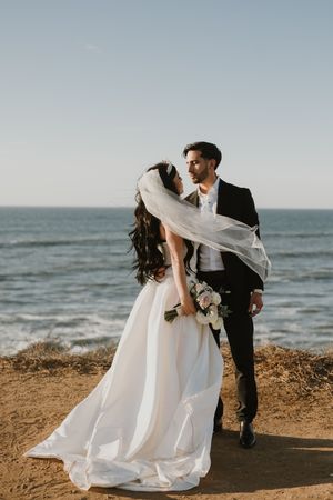 Romantic coastal wedding photos with couple posing against ocean backdrop at sunset.
