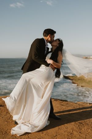 Dramatic wedding poses on coastal cliffs with ocean waves in background.