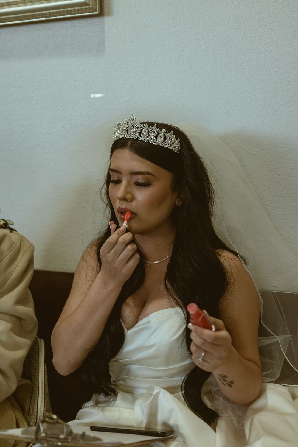 Bride wearing tiara and veil applies lipstick while getting ready for wedding.