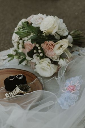 Elegant wedding details featuring white roses, rings and veil on a wooden surface.