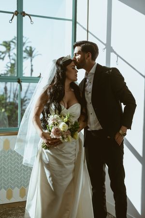 Elegant wedding couple shares intimate moments in a bright modern venue with large windows.