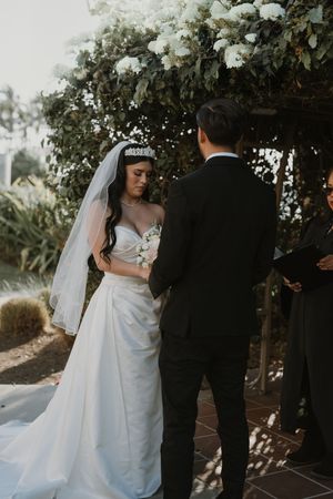 Wedding couple poses under blooming white flowers in an outdoor garden setting.
