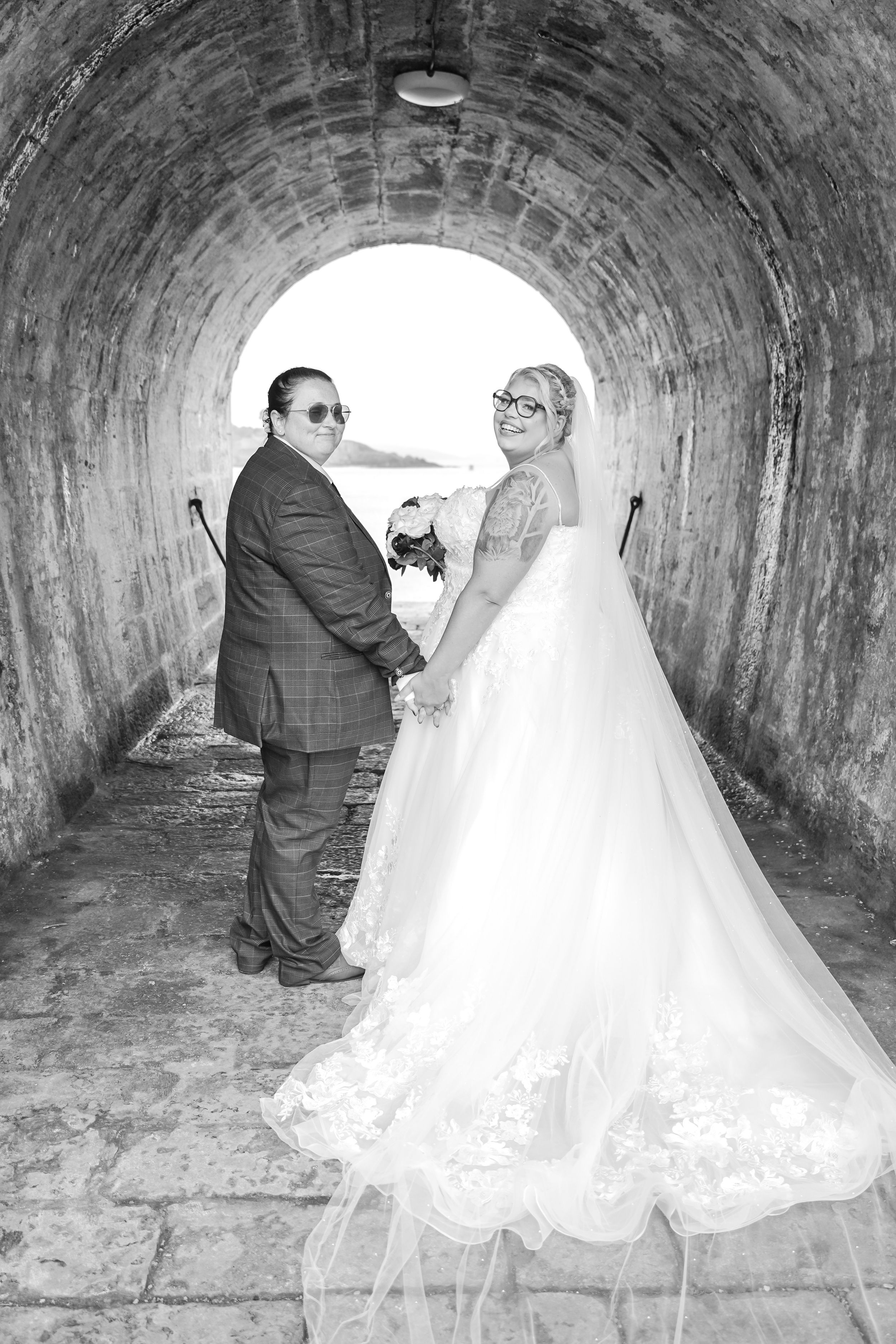 A couple poses in black and white photography inside a stone tunnel on their wedding day.