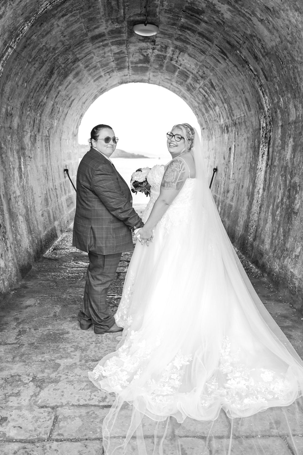 A couple poses in black and white photography inside a stone tunnel on their wedding day.