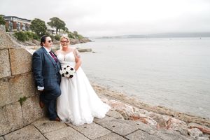 Scenic wedding photography along a rocky coastal shoreline with overcast skies and calm waters in the background.