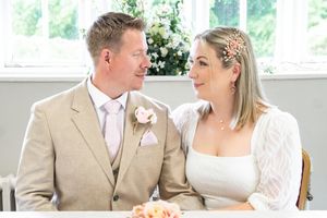 A newlywed couple in light colored wedding attire sit close together and share a tender moment during their wedding day.