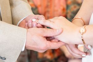 Close up of hands exchanging wedding rings during marriage ceremony with orange floral background.