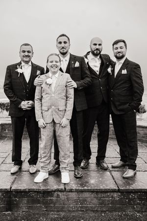 Black and white wedding photo showing men in dark suits and a young person in light overalls standing together on stone steps.