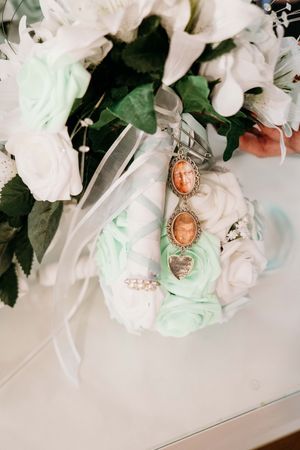 Vintage cameo earrings hanging from mint and white roses in a romantic wedding bouquet.