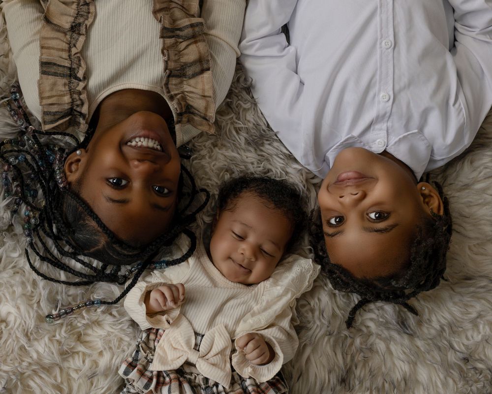 Three people lying on a plush carpet wearing white outfits seen from above in a heartwarming intimate portrait.